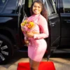 A woman in a pink dress stands beside a sleek black car, showcasing a stylish and elegant scene.