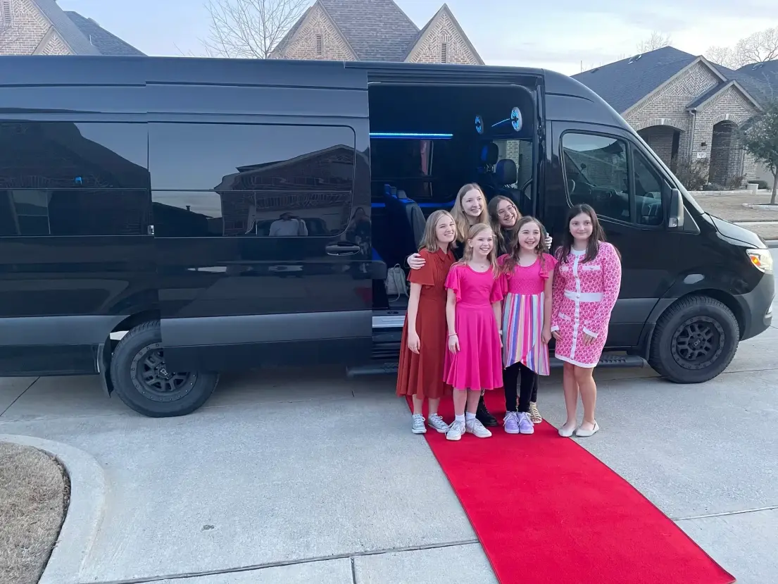 A group of girls poses together in front of a black van, smiling and enjoying their time together.