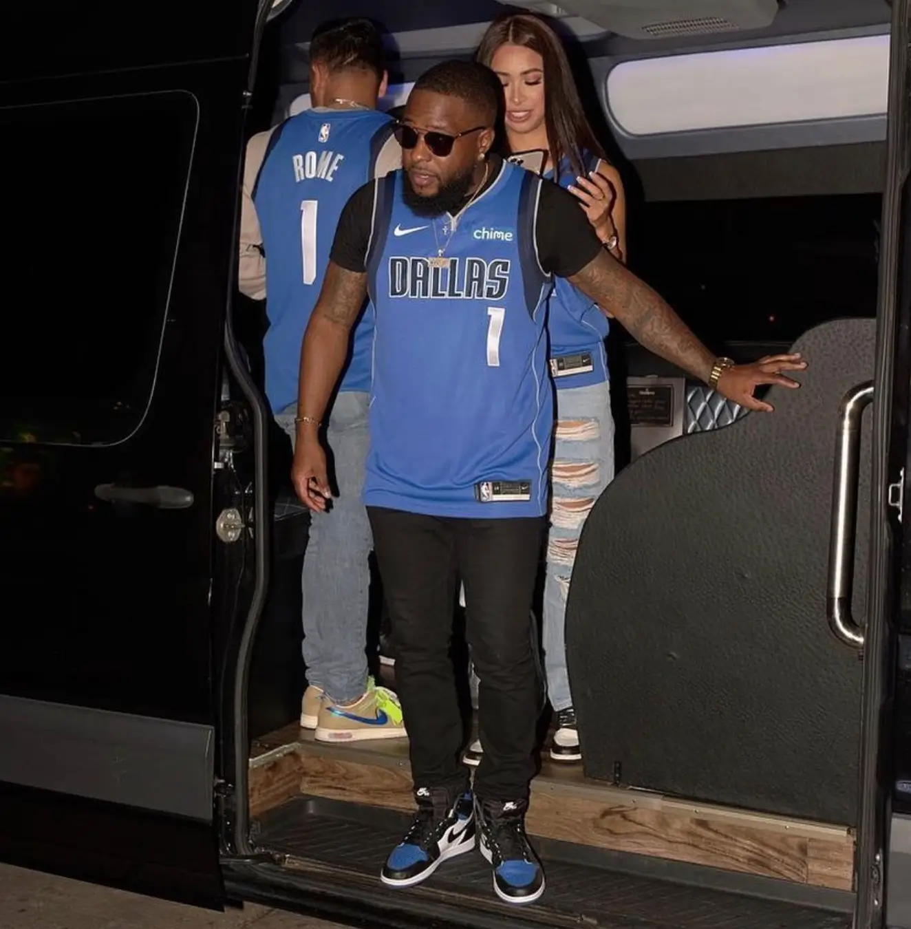 A man and woman standing together in the back of a van, engaged in conversation or enjoying their surroundings.