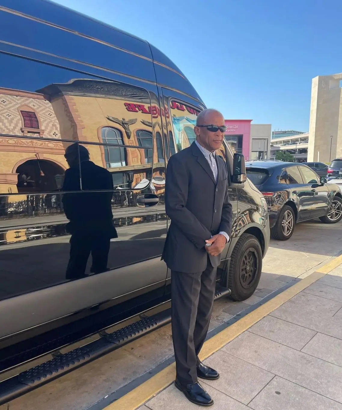 A man in a suit stands beside a black van, exuding professionalism and readiness for business.