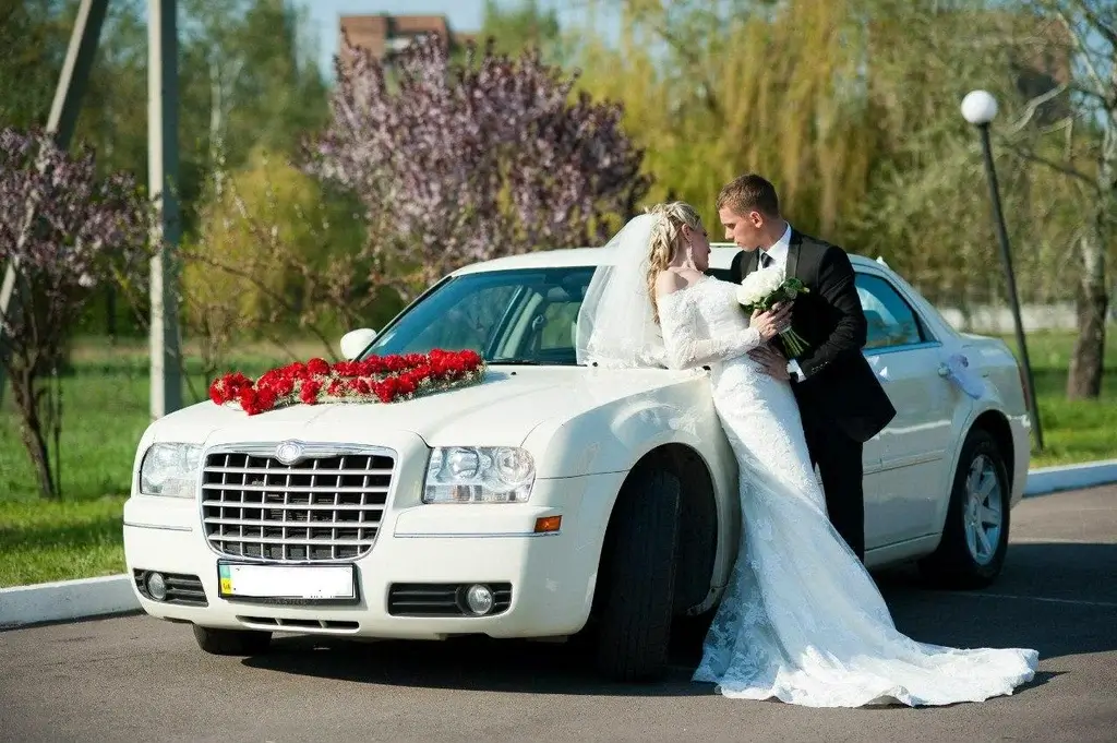 A bride and groom pose happily beside a luxurious white limousine on their wedding day.