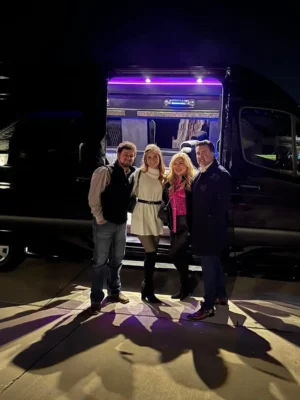 Three individuals standing in front of a black van under the night sky, illuminated by ambient street lighting