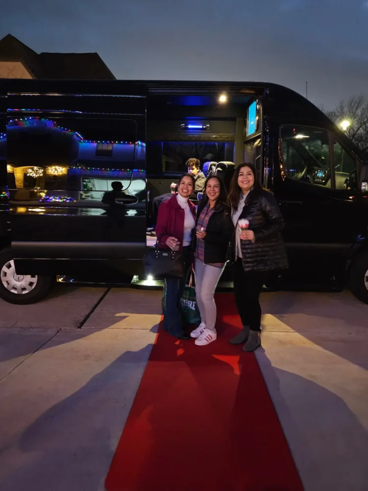 Three women pose together in front of a sleek black bus, smiling and enjoying their time outdoors.